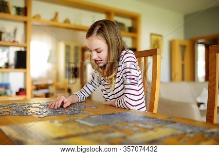 Cute Young Girl Playing Puzzles At Home. Child Connecting Jigsaw Puzzle Pieces In A Living Room Tabl
