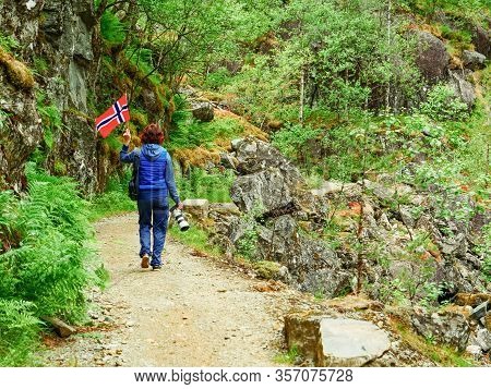 Tourist Woman With Norwegian Flag And Camera Walking Trough Mountains Path In Allmannajuvet Area Sau