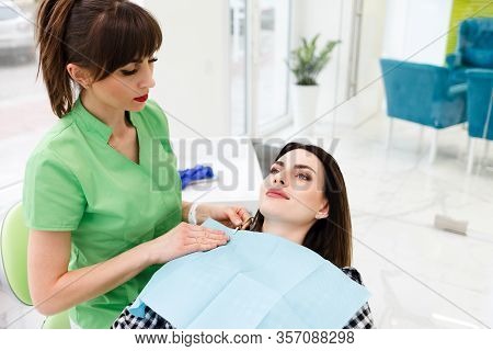 Dentist Doctor Puts Dental Napkin On Patient. Preparing The Patient For A Dental Examination