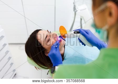 Girl Treats Teeth At The Dentistry. Dentist Using Dental Curing Uv Lamp On Teeth Of Patient