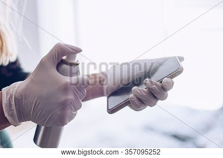 Woman Disinfects The Phone With A Spray Disinfectant Liquid.