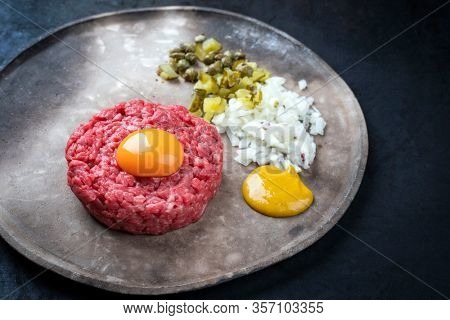 Gourmet tartar raw from beef fillet with yellow of the egg, gherkin and capers as closeup on a modern design rustic plate 
