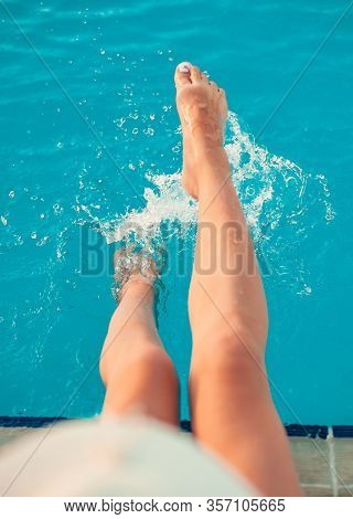 Stylish Girl In White Hat Sittting On Wooden Deck Chair Near The Pool Outdoors. Relax And Having Fun