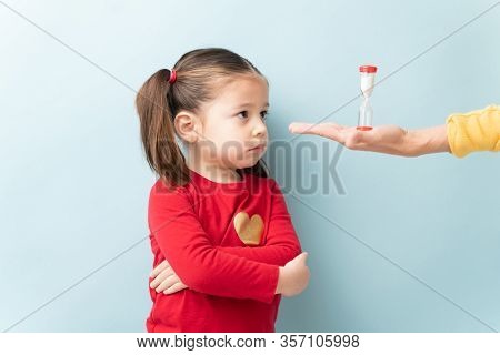 Hand Of A Parent Holding A Sand Timer In Front Of A Little Girl While She Is On Timeout