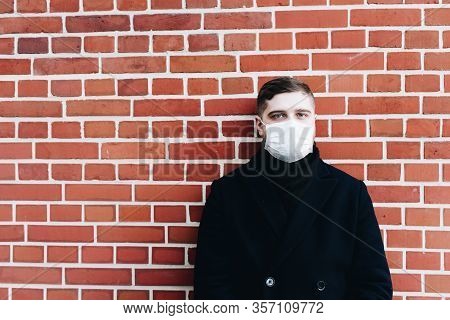 Young Caucasian Man With Surgical Mask To Protect From Coronavirus On A Brick Wall Background With C