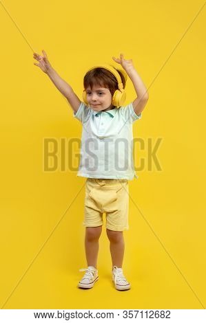 Full Lengh Photo Of Funny Kid Listening Music In Headphone And Dance With Hands Up Over Yellow Backg
