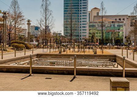 Daejeon, South Korea; March 16, 2020: Dry Water Fountain In City Park With Buildings In Background L