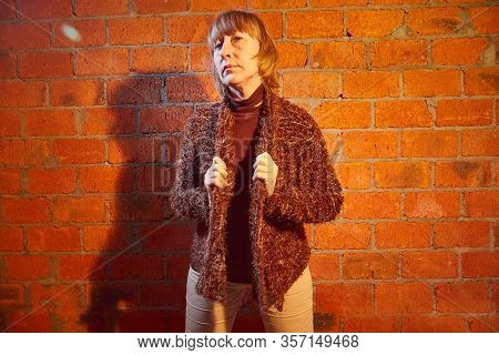A Middle-aged Woman Poses Showing Clothes Near Red Brick Wall. An Inept Model In An Inept Shoot