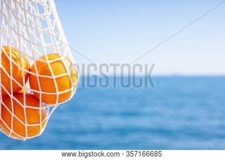 White Cotton Eco String Bag With Oranges. Sea View With A Blue Sky. Zero And Eco Waste. No Plastic. 