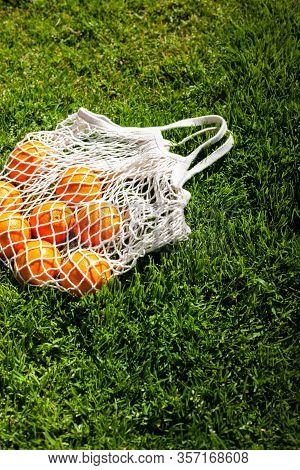 White Cotton Eco String Bag With Oranges On A Grass. Good Idea For A Picnic. Zero And Eco Waste. No 