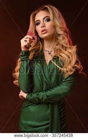 Blonde Female, Bright Make-up, Green Stylish Dress And Jewelry. Showing Two Red Chips, Propping Her 