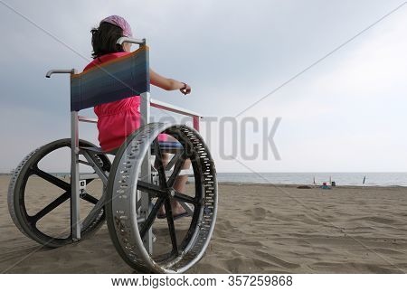Girl In A Wheelchair Points To The Sea From The Beach