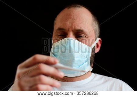 A Man In A Medical Mask Holds A Thermometer In His Hand. Bokeh. Selective Focus.