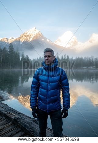 Man Standing At A Mountain Lake Enjoying The Sunrise In The Austrian Alps