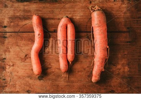 Ugly Misshapen Carrots On Wooden Background. Concept Of Zero Waste Production. Top View. Copy Space.