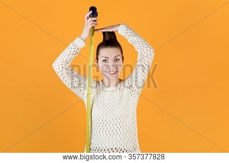 Smiling Girl Holds Measuring Tape Next To Her And Measures Her Height, Isolated On Orange-yellow