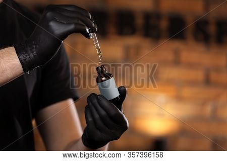 Man Holding Essential Oil For Beard In Glass Bottle On Hand And Dripping Oil. Man With Black Gloves 