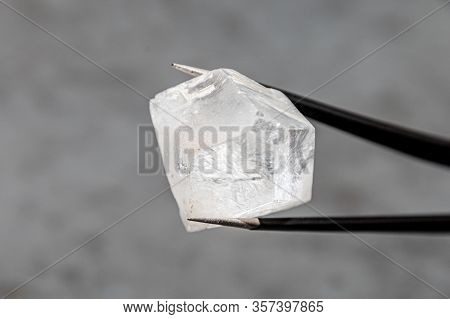 Raw Diamond Big Dob Held By Tweezers In Front Of Grey Surface