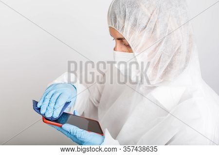 Woman In Protective Gloves And Siut Cleaning Her Phone From Dust And Infection On White Background