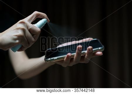 Hand Holding And Cleaning Mobile Phone Screen With Isopropyl Alcohol Spray  For Corona Virus Or Covi
