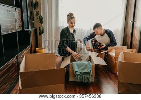 Couple Holding Moving Boxes In New Home. Moving Day, New Home, Unpacking Boxes, Newlyweds Concept