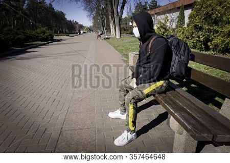 Sick Caucasian Young Man Sitring Alone On A Bench At The Public Park At Quarantine In A Protective F