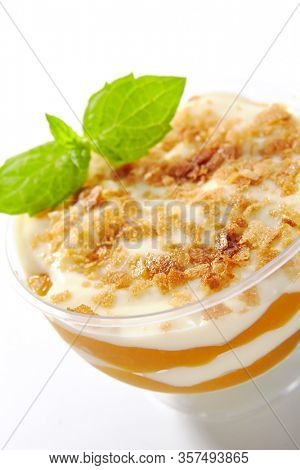 Dessert with mango, vanilla cream and cookie crumbs in restaurant glass isolated. Delicious fruit blancmange with apricots, prepared panna cotta or creamy mousse on white table closeup