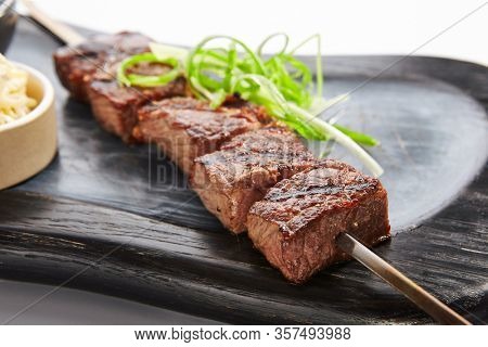 Marbled beef skewer closeup view. Delicious kebab with sauce and noodles on wooden tray. Grilled meat with tasty garnish. Spicy meal with onion. Restaraunt dish, roasted food composition
