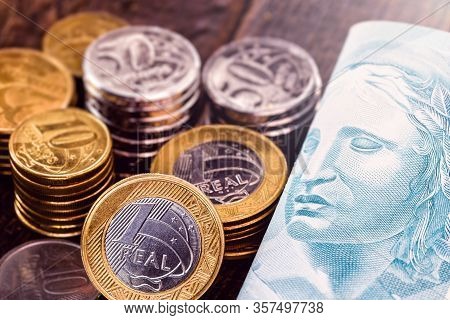 Money And Banknotes Of 100 Reais From Brazil, Coins From One Real On A Well Lit Rustic Wooden Backgr