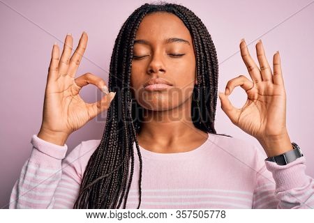 Close up of young african american woman wearing pink sweater over isolated background relax and smiling with eyes closed doing meditation gesture with fingers. Yoga concept.