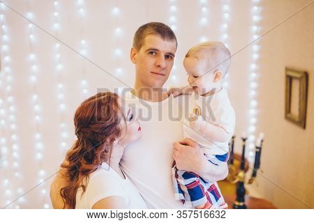 Dad And Moma Holds The Baby In His Arms. Boy Eating Bagel. The Concept Of Educating The Father Of Yo