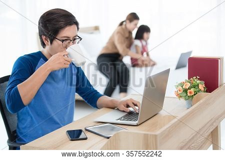 Asian Businessman Drink Coffee While Working At Home With Computer, Tablet, And Smartphone While His