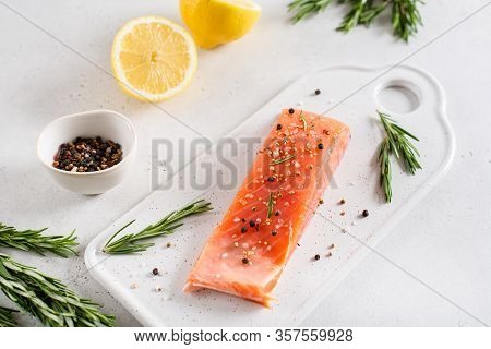 Fresh Raw Salmon Fillet On White Stone Board With Salt, Peppers, Lemon, And Rosemary On White Backgr