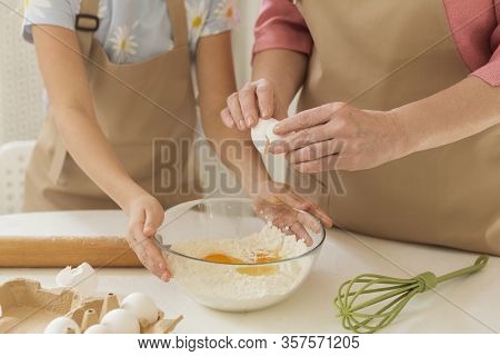 Family Cooking Time. Maure Lady Adding Egg To Flour While Little Girl Helping Her In Kitchen, Closeu