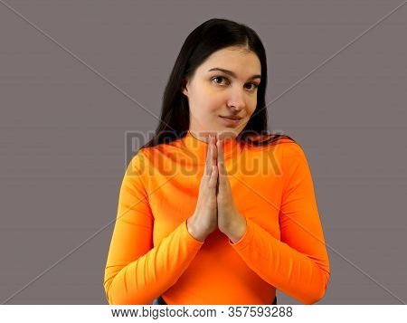 Young Beautiful Girl With Dark Hair In A Bright Orange Sweater On A Gray Background. Implore