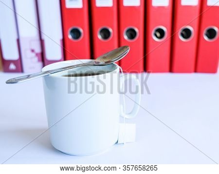 Tea At The Office. White Ceramic Mug With Tea On The Background Of Red Office Folders For Documents.