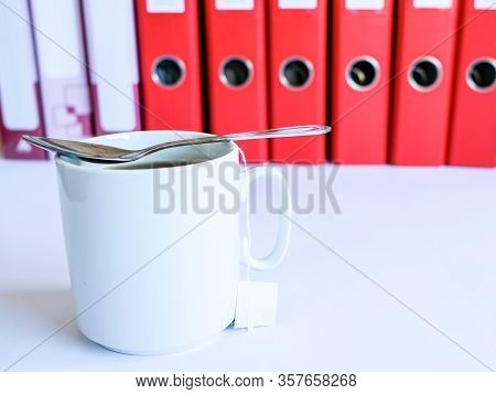 Tea At The Office. White Ceramic Mug With Tea On The Background Of Red Office Folders For Documents.
