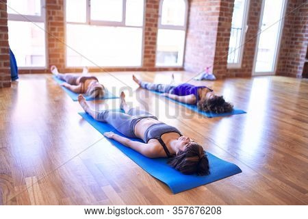 Young beautiful group of sportswomen practicing yoga. Lying down doing corpse pose at gym