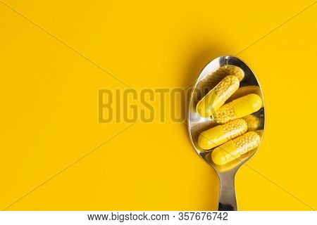 Vitamin capsules. Vitamin C pills in spoon on yellow background. Top view.