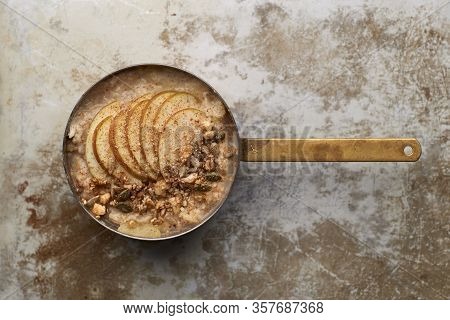 Oatmeal Topped With Apple Slices And Granola Sprinkled With Cinammon Powder In Copper Pot Overhead V