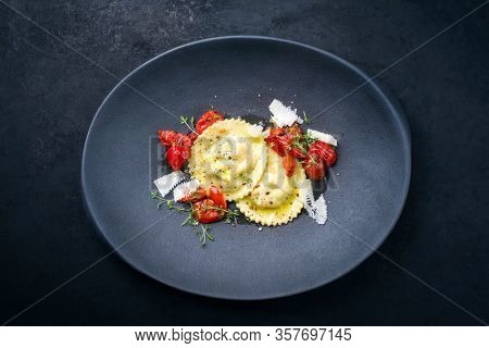 Traditional Italian ravioli pasta offered with parmesan cheese and fried tomatoes as top view on a modern design plate with copy space 