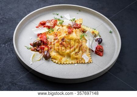 Traditional Italian ravioli pasta offered with parmesan cheese, fried tomatoes and olives as closeup on a modern design plate 