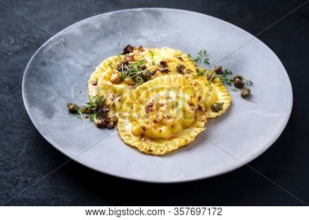 Traditional Italian ravioli pasta offered with capers and onion chili pesto closeup on a modern design plate 