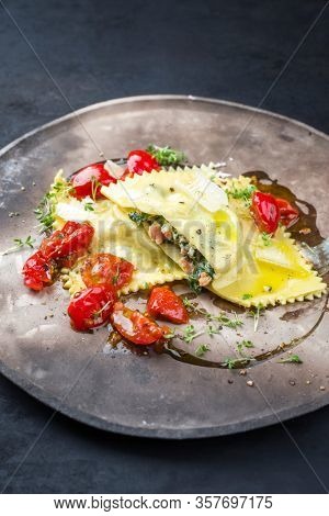 Traditional Italian ravioli pasta offered with salmon spinach filling and fried tomatoes as closeup on a modern design plate 