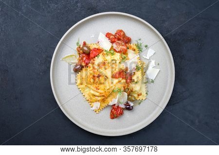 Traditional Italian ravioli pasta offered with parmesan cheese, fried tomatoes and olives as top view on a modern design plate with copy space 