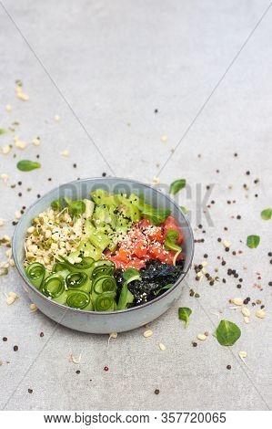 Salted Salmon Poke Bowl With Avocado, Sea Cale, Cucumber, Sesame Seeds And Bean Sprouts On Grey Back