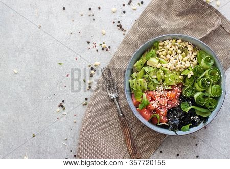 Salted Salmon Poke Bowl With Avocado, Sea Cale, Cucumber, Sesame Seeds And Bean Sprouts On Grey Back
