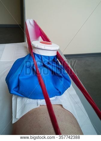 Rehabilitation With Elastic Red Band And Ice On The Knee On The Physiotherapy Bed Within A Medical C