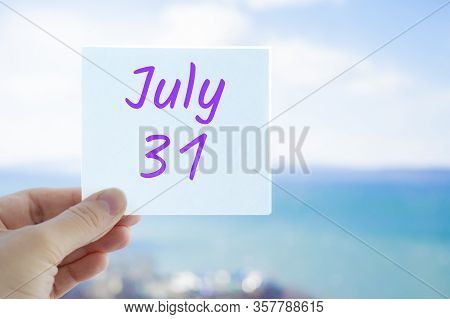 July 31st. Hand Holding Sticker With Text July 31 On The Blurred Background Of The Sea And Sky. Copy