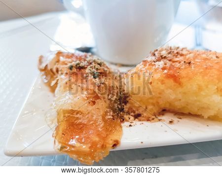 Delicious Greek sweet pastry named Galaktoboureko, made of semolina custard in filo, served with honey in white plate.